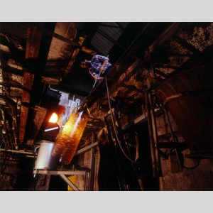 Souffleur de verre tenant la canne à bout de bras pour allonger le manchon par un mouvement de balancier dans la fosse à la Verrerie de Saint-Just, 1994